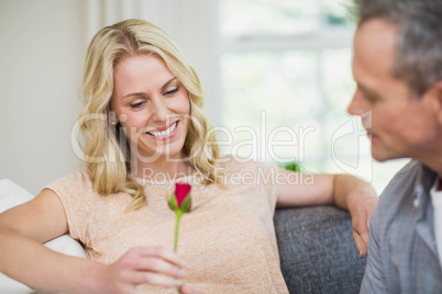 Pretty woman sitting on her couch and husband offering a rose