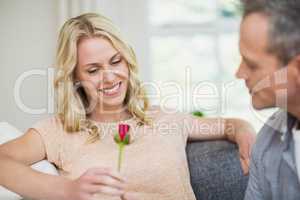 Pretty woman sitting on her couch and husband offering a rose