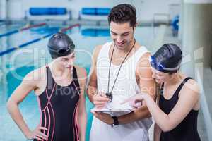 Smiling trainer showing clipboard at swimmers