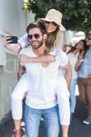 Hip man giving piggy back to his girlfriend and taking selfie