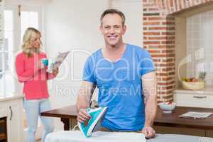 Man ironing while wife reading the news