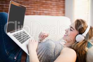 Pretty woman lying on the couch using her laptop and listening m