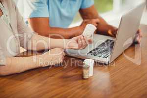 Senior couple using laptop and holding pills