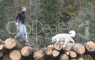 Young man and dog on logs in the forest