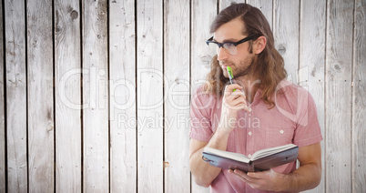Composite image of thoughtful hipster holding pen and book