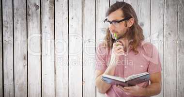 Composite image of thoughtful hipster holding pen and book