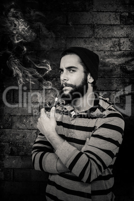 Composite image of portrait of serious hipster smoking pipe