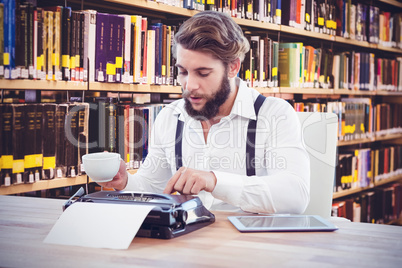 Composite image of hipster holding coffee working on typewriter