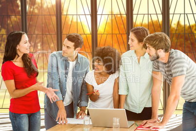 Composite image of colleagues gathered around a laptop at office