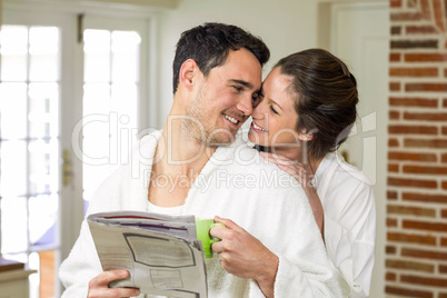 Couple cuddling while having tea and reading newspaper