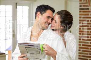 Couple cuddling while having tea and reading newspaper