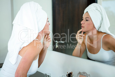 woman wearing a  hair towel inspecting her skin