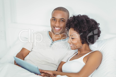 Smiling couple at bed using tablet