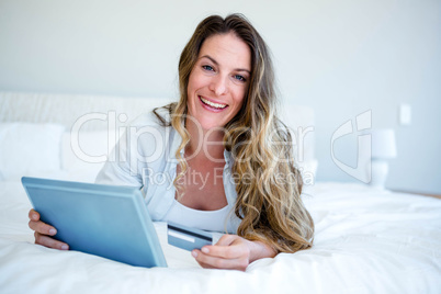 woman lying on her tablet holding her credit card