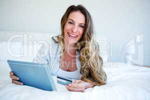 woman lying on her tablet holding her credit card