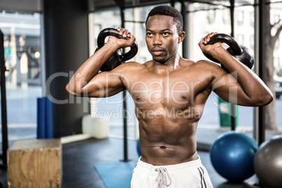 Shirtless man lifting heavy kettlebells