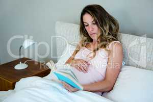 tired pregnant woman lying in bed reading