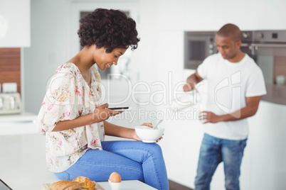 Happy couple eating breakfast and using smartphone