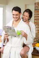 Young couple in bathrobe having tea and reading newspaper