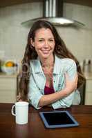 Young woman in kitchen with coffee mug and digital tablet on wor