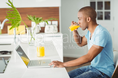 Smiling man using laptop and drinking orange juice