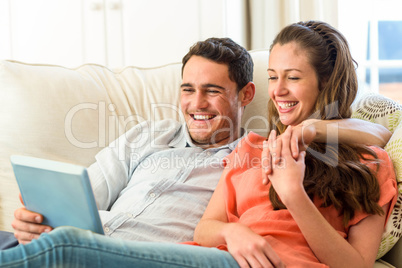 Young couple having fun while using digital tablet on sofa