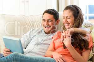 Young couple having fun while using digital tablet on sofa