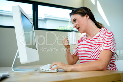 smiling woman sipping coffee at her desk