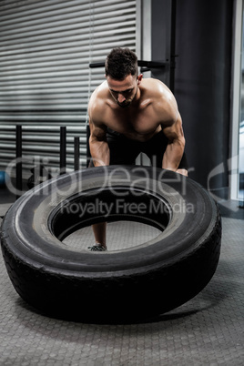 Shirtless man flipping heavy tire