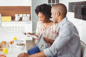 Smiling couple reading magazine and documents during breakfast