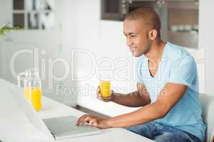 Smiling man using laptop and drinking orange juice