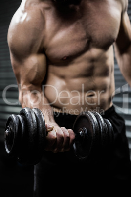 Mid section of shirtless man lifting heavy dumbbell