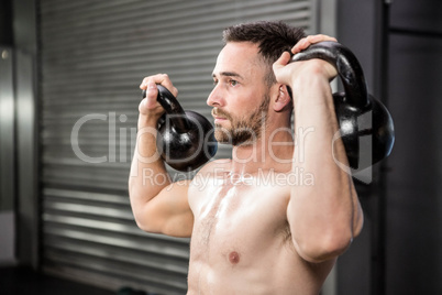 Shirtless man lifting kettlebells