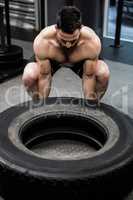 Shirtless man flipping heavy tire