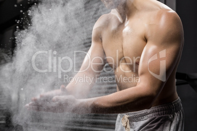 Mid section of shirtless man clapping hands with talc