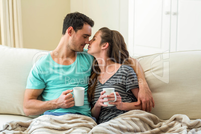 Young couple cuddling on sofa while having coffee