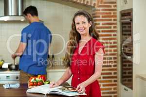 Woman checking the recipe book and man cooking on stove