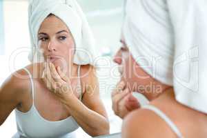 woman wearing a  hair towel inspecting her skin