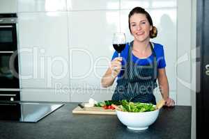 smiling woman preparing vegetables and drinking red wine