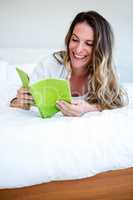 smiling woman lying on her bed reading a book