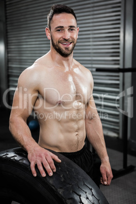 Smiling shirtless man standing next to heavy tire