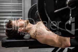 Shirtless man lifting heavy barbell on bench