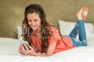 Young woman lying on bed with her phone