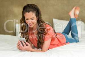 Young woman lying on bed with her phone