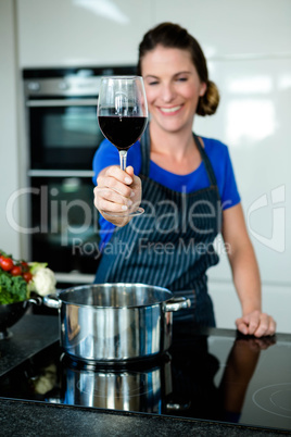 smiling woman cooking on the stove top and drinking red wine