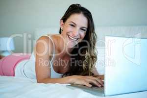 smiling woman lying on her bed with her laptop