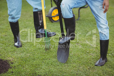 Lower section of couple holding shovel and rake