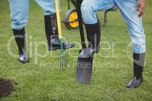 Lower section of couple holding shovel and rake