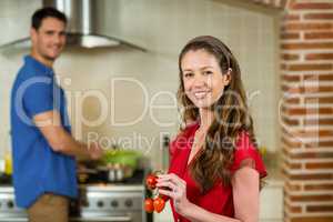Woman holding cherry tomato and man cooking on stove