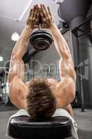 Shirtless man lifting heavy dumbbell on bench